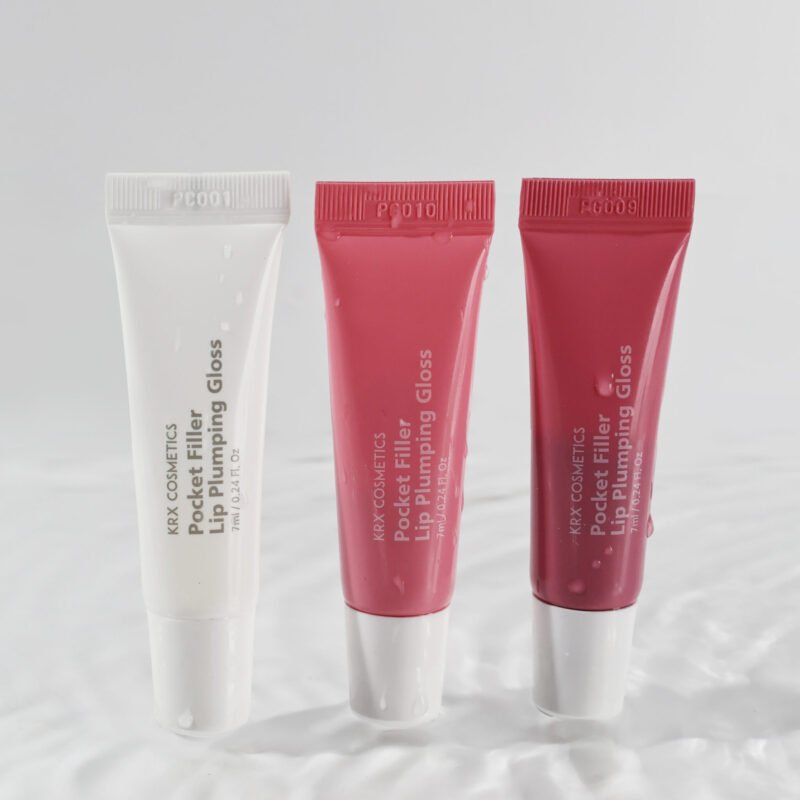 Drei Tuben KRX COSMETICS Pocket Filler Lip Plumping Gloss in den Farben Transparent, Rosé und Rot – auf glänzendem Hintergrund stehend.